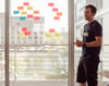 Bild zeigt einen Mann, der vor eine Glasfront steht auf der mehrere Post-its hängen. Im Hintergrund sieht man den Duisburger Innenhafen.