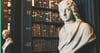 Auf dem Bild ist eine steinerne Statue in einer Bibliothek zu sehen.